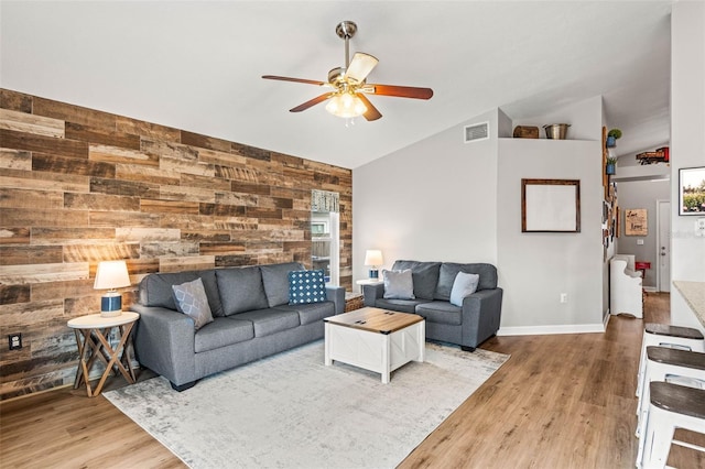 living room with vaulted ceiling, ceiling fan, light hardwood / wood-style flooring, and wood walls