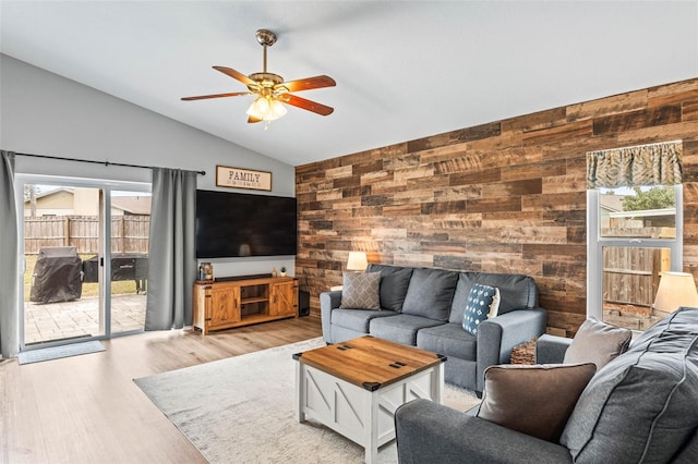 living room with lofted ceiling, ceiling fan, wooden walls, and light hardwood / wood-style floors