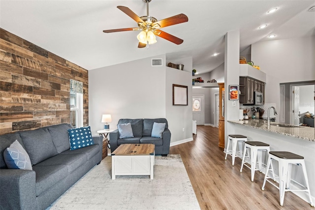 living room featuring wooden walls, sink, vaulted ceiling, ceiling fan, and light hardwood / wood-style flooring