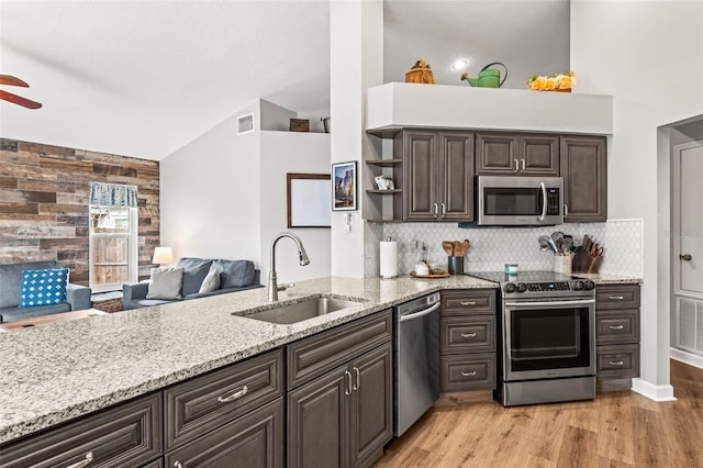 kitchen featuring appliances with stainless steel finishes, wooden walls, sink, ceiling fan, and dark brown cabinets