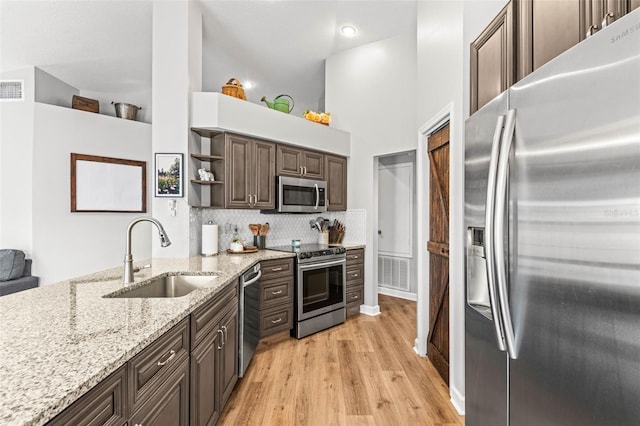 kitchen with appliances with stainless steel finishes, sink, high vaulted ceiling, light stone counters, and dark brown cabinets