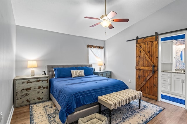 bedroom with light wood-type flooring, ceiling fan, a barn door, and ensuite bath