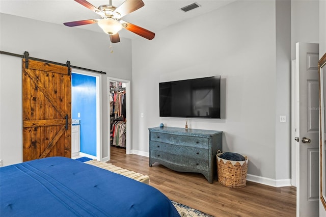 bedroom with a spacious closet, a barn door, hardwood / wood-style flooring, ceiling fan, and a closet