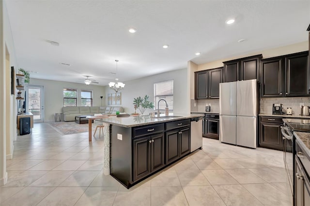 kitchen with appliances with stainless steel finishes, sink, hanging light fixtures, a kitchen island with sink, and light stone counters