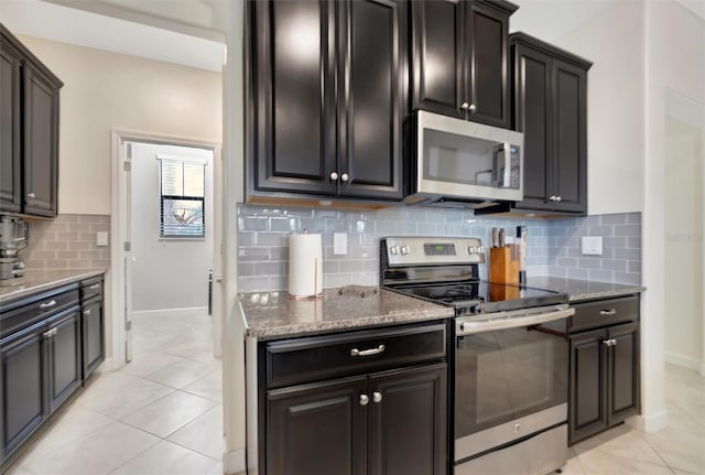 kitchen with light tile patterned flooring, stainless steel appliances, dark stone countertops, and decorative backsplash