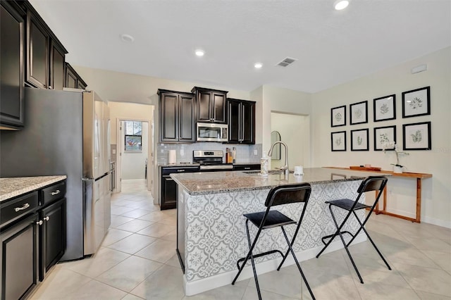 kitchen featuring stainless steel appliances, a center island with sink, and light stone countertops