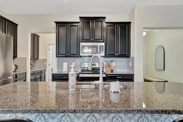 kitchen with light stone counters, an island with sink, appliances with stainless steel finishes, and tasteful backsplash