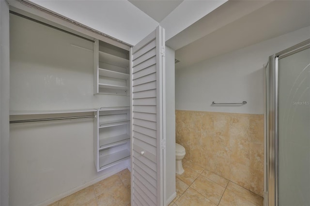 bathroom featuring toilet, a shower with door, and tile patterned flooring