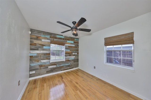 empty room featuring hardwood / wood-style flooring, wooden walls, and ceiling fan