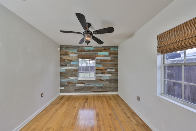 unfurnished room with ceiling fan, wood walls, and light wood-type flooring