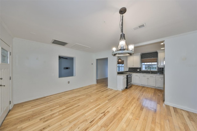 kitchen with hanging light fixtures, stainless steel electric range, sink, white cabinets, and backsplash