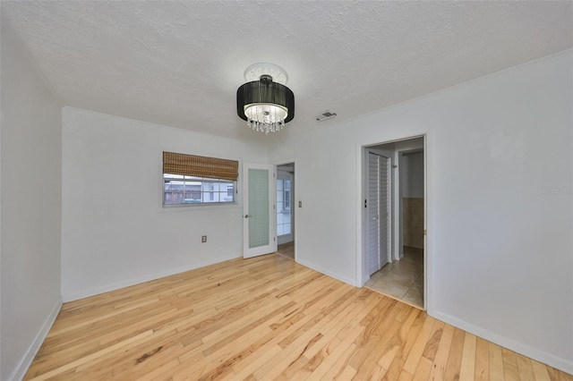 unfurnished room with light wood-type flooring, a textured ceiling, and an inviting chandelier