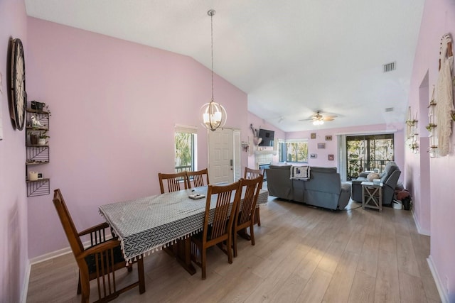 dining area featuring ceiling fan with notable chandelier, vaulted ceiling, and light wood-type flooring