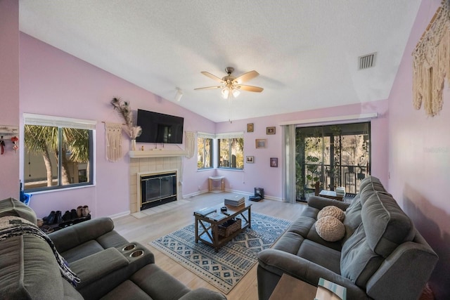 living room featuring vaulted ceiling, a textured ceiling, a fireplace, and light wood-type flooring