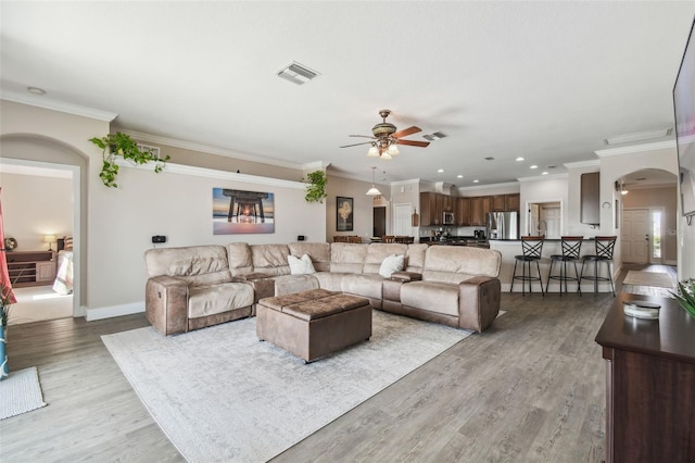 living room with crown molding, ceiling fan, and light wood-type flooring