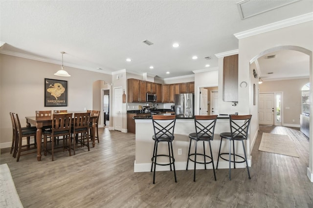 kitchen with a breakfast bar area, appliances with stainless steel finishes, wood-type flooring, decorative light fixtures, and kitchen peninsula