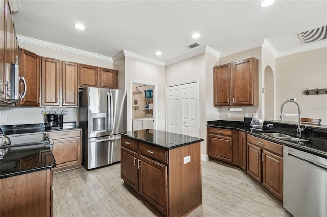 kitchen with appliances with stainless steel finishes, sink, a center island, washing machine and clothes dryer, and light hardwood / wood-style flooring