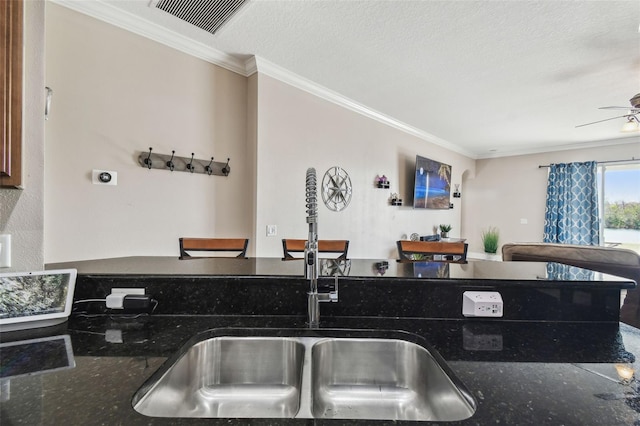 kitchen featuring crown molding, ceiling fan, dark stone counters, and sink