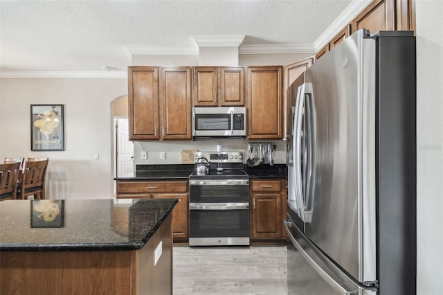 kitchen featuring crown molding, a textured ceiling, light hardwood / wood-style flooring, dark stone countertops, and stainless steel appliances