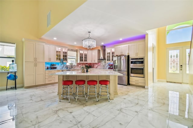 kitchen with backsplash, wall chimney range hood, a kitchen island, sink, and appliances with stainless steel finishes