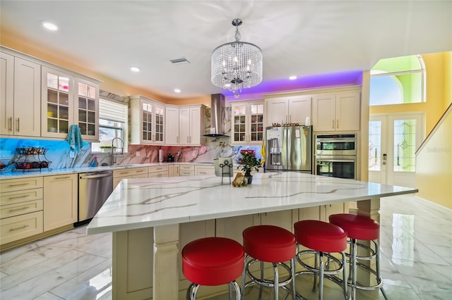 kitchen featuring stainless steel appliances, backsplash, a spacious island, wall chimney range hood, and pendant lighting