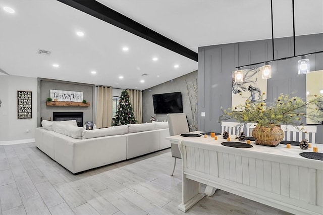 living room with a large fireplace, light hardwood / wood-style floors, and vaulted ceiling with beams