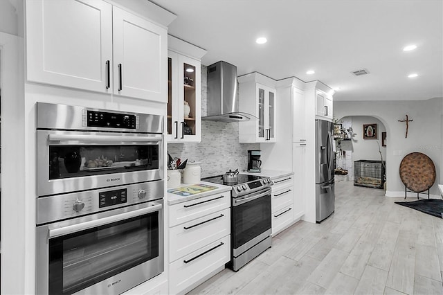 kitchen featuring white cabinetry, wall chimney range hood, decorative backsplash, and stainless steel appliances