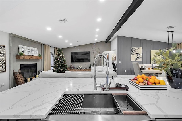 kitchen featuring gray cabinetry, a large fireplace, pendant lighting, light stone counters, and lofted ceiling with beams