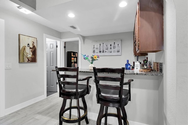 bar with light hardwood / wood-style floors and dark stone countertops