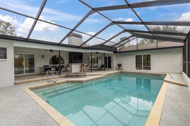 view of swimming pool with ceiling fan, exterior bar, a patio area, and glass enclosure