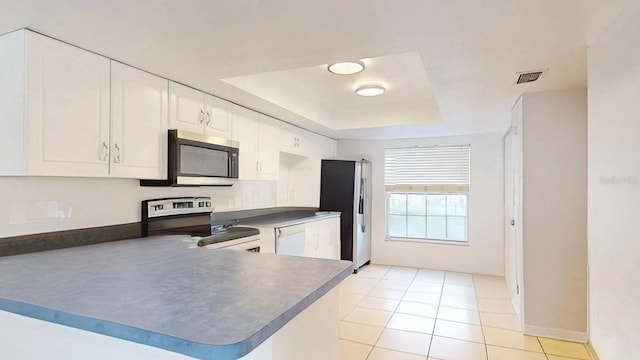 kitchen featuring appliances with stainless steel finishes, white cabinetry, light tile patterned floors, kitchen peninsula, and a tray ceiling