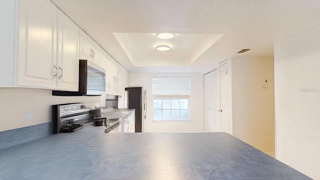 kitchen featuring kitchen peninsula, white cabinets, a raised ceiling, and stove