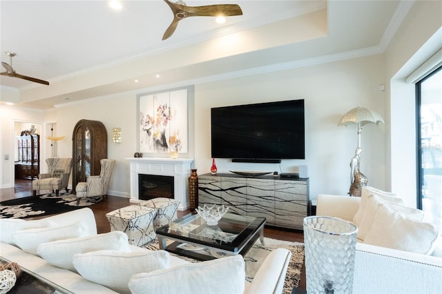 living room with wood-type flooring, ornamental molding, ceiling fan, and a tray ceiling