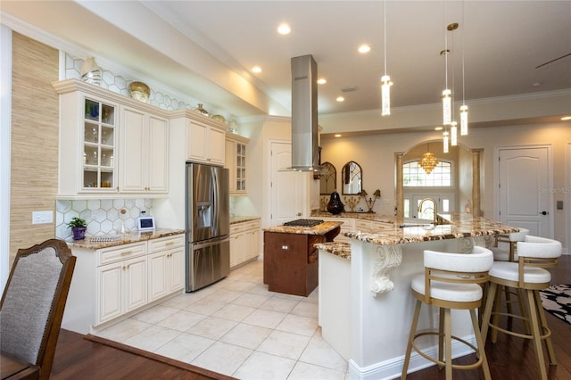 kitchen with a spacious island, hanging light fixtures, appliances with stainless steel finishes, island exhaust hood, and light stone countertops