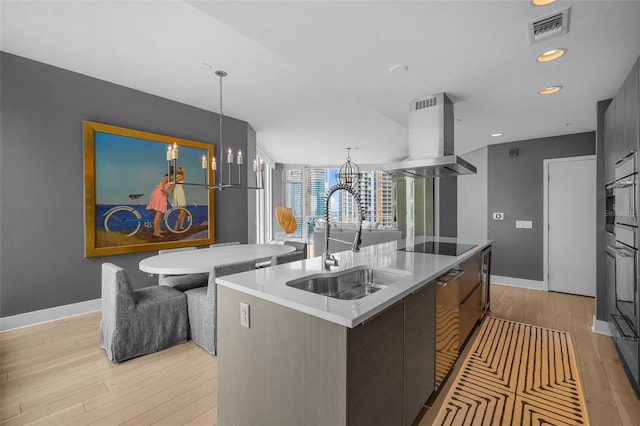 kitchen with pendant lighting, island exhaust hood, light hardwood / wood-style floors, sink, and a kitchen island with sink