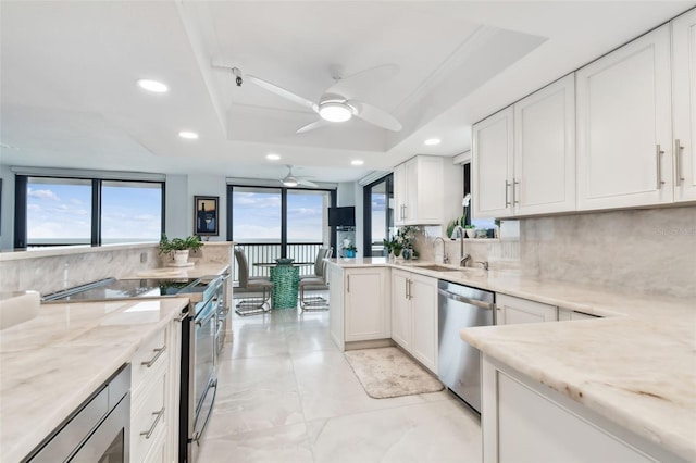 kitchen featuring light stone counters, a sink, a tray ceiling, stainless steel appliances, and backsplash