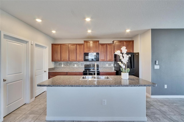 kitchen featuring light tile patterned floors, sink, backsplash, black appliances, and a center island with sink