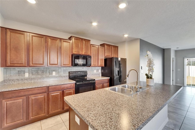 kitchen with sink, light tile patterned floors, a kitchen island with sink, decorative backsplash, and black appliances