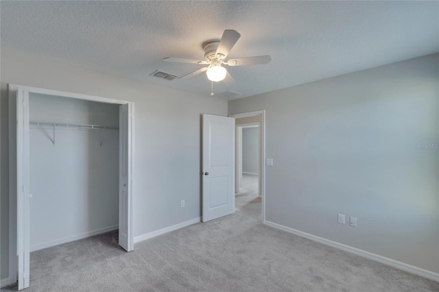 unfurnished bedroom featuring ceiling fan, a closet, light carpet, and a textured ceiling