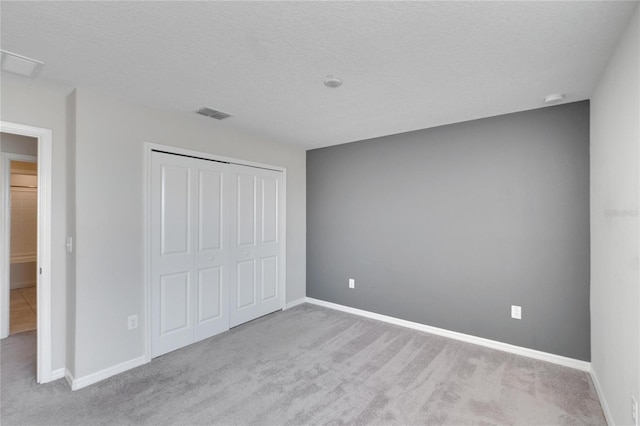 unfurnished bedroom featuring light carpet, a closet, and a textured ceiling