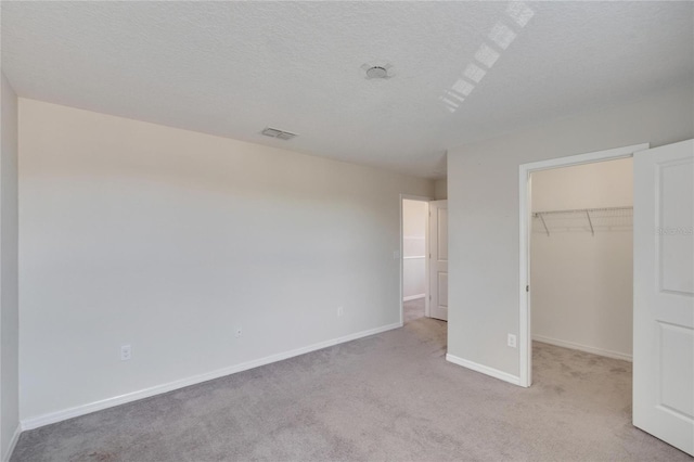 unfurnished bedroom featuring carpet, a spacious closet, and a textured ceiling