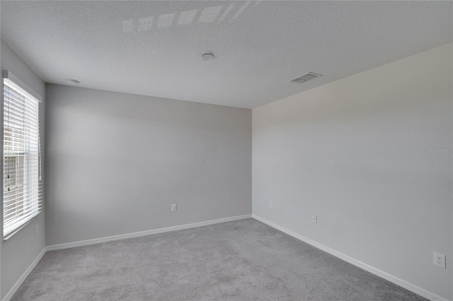 carpeted empty room featuring baseboards, visible vents, and a textured ceiling