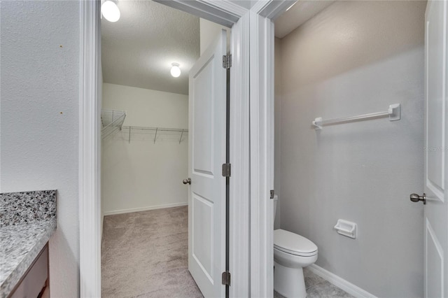 bathroom with a walk in closet, baseboards, vanity, and toilet