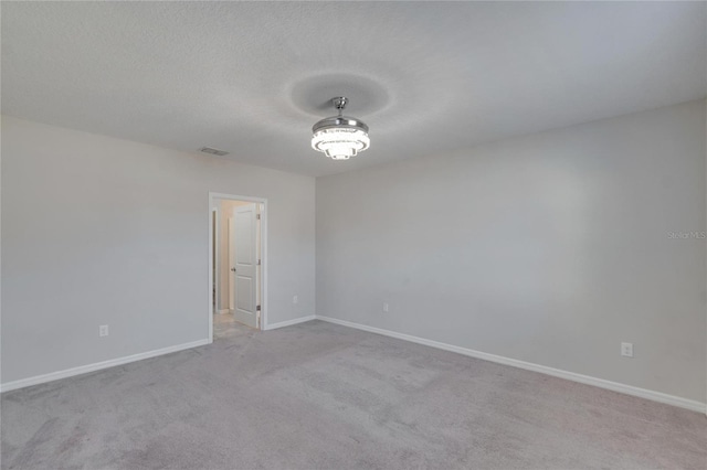 carpeted spare room with baseboards, visible vents, and a textured ceiling