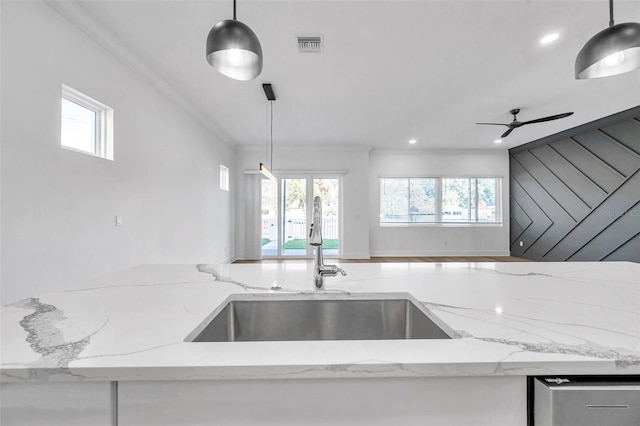 kitchen with ceiling fan, sink, hanging light fixtures, light stone countertops, and ornamental molding