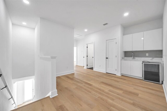 kitchen featuring wine cooler, backsplash, sink, white cabinetry, and light hardwood / wood-style flooring