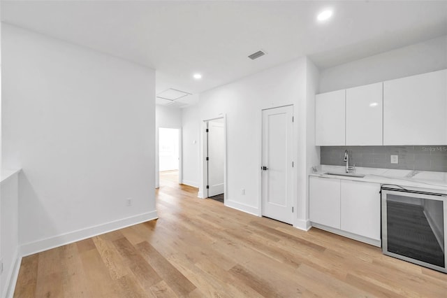 kitchen featuring white cabinetry, backsplash, light wood-type flooring, beverage cooler, and sink