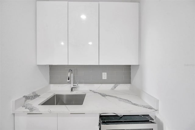 kitchen with tasteful backsplash, white cabinets, light stone countertops, and sink