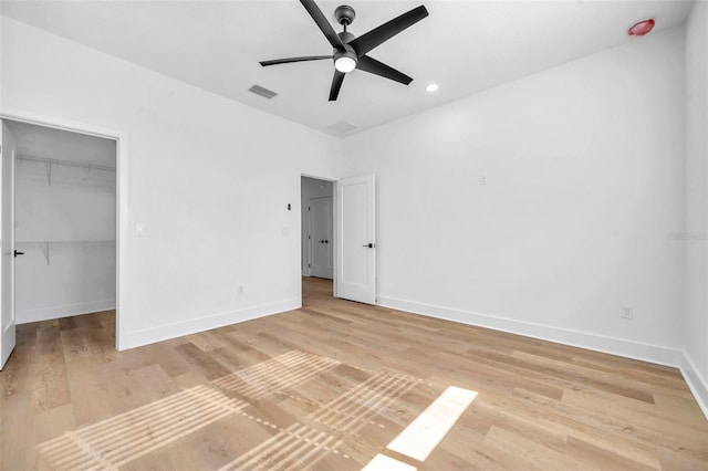 unfurnished bedroom featuring ceiling fan, wood-type flooring, a closet, and a walk in closet