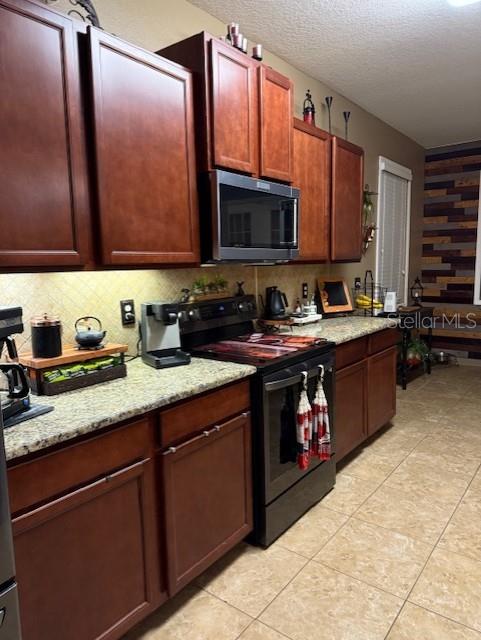 kitchen with light tile patterned floors, tasteful backsplash, a textured ceiling, light stone counters, and black range with electric stovetop